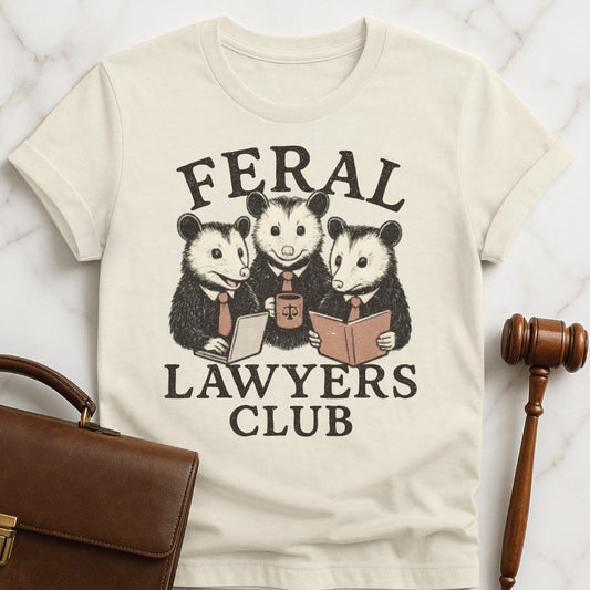 funny law school grad t shirt that says feral lawyers club featuring three possums in business suits and a briefcase in cream