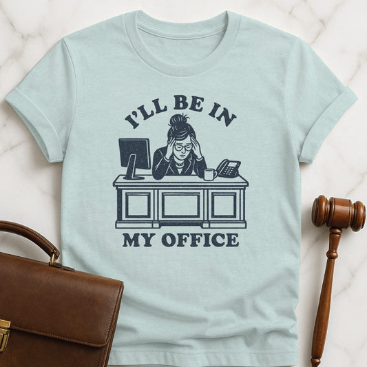 cool new lawyer graphic t shirt that says Ill be in my office featuring woman lawyer slumped over her desk looking stressed out in heather blue