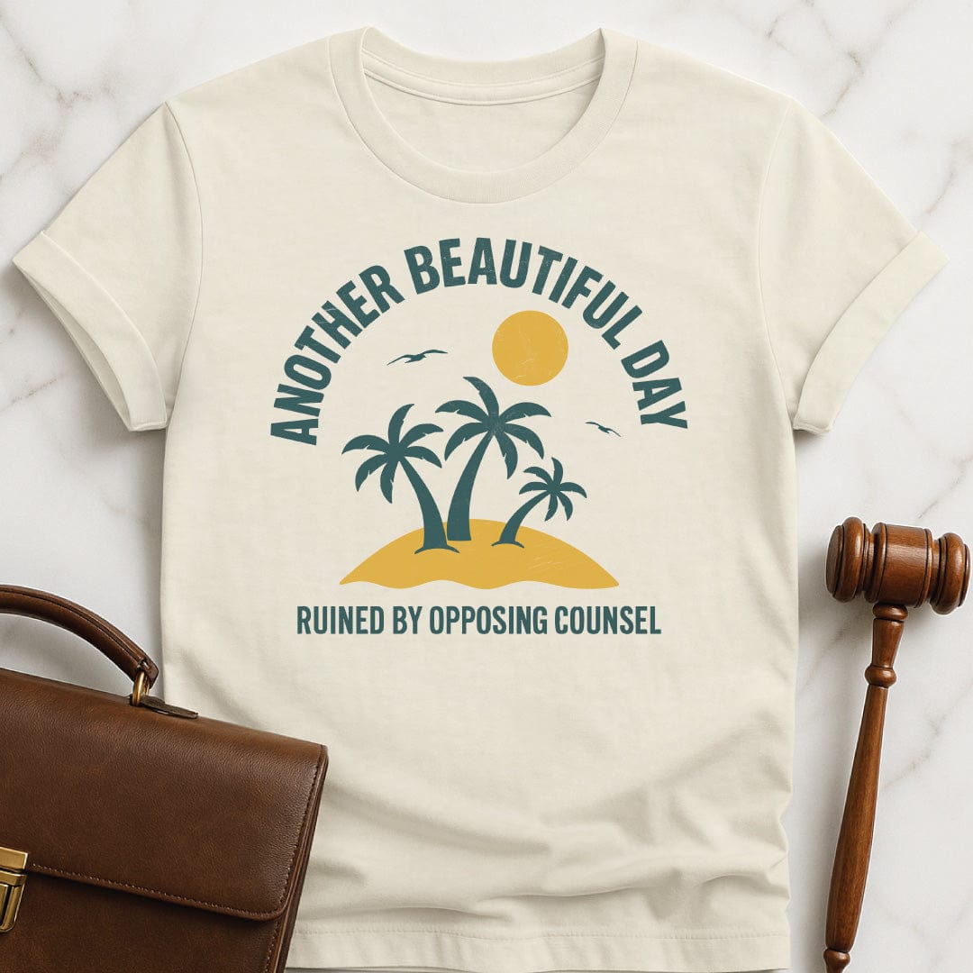 clever new lawyer graphic t shirt that says Another beautiful day ruined by opposing counsel featuring palm trees on a tropical island with sun and birds in cream
