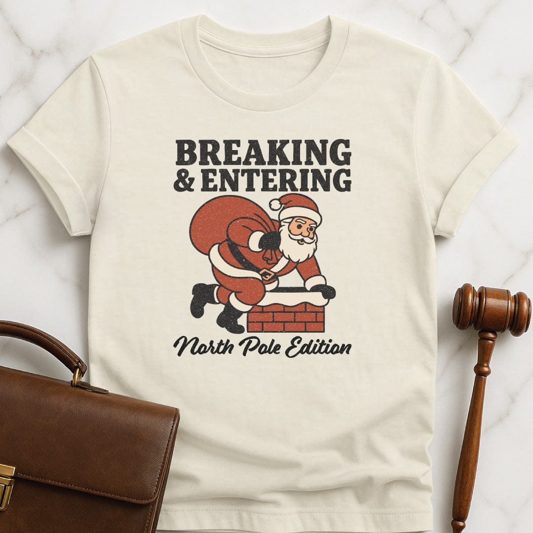 santa law grad graphic tee that says Breaking and entering North Pole edition featuring Santa Claus going down a chimney in cream