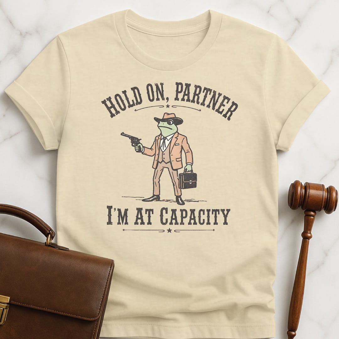 cool lawyer t-shirt that says Hold on partner Im at capacity featuring cowboy lawyer toad or frog holding a gun and briefcase in cream