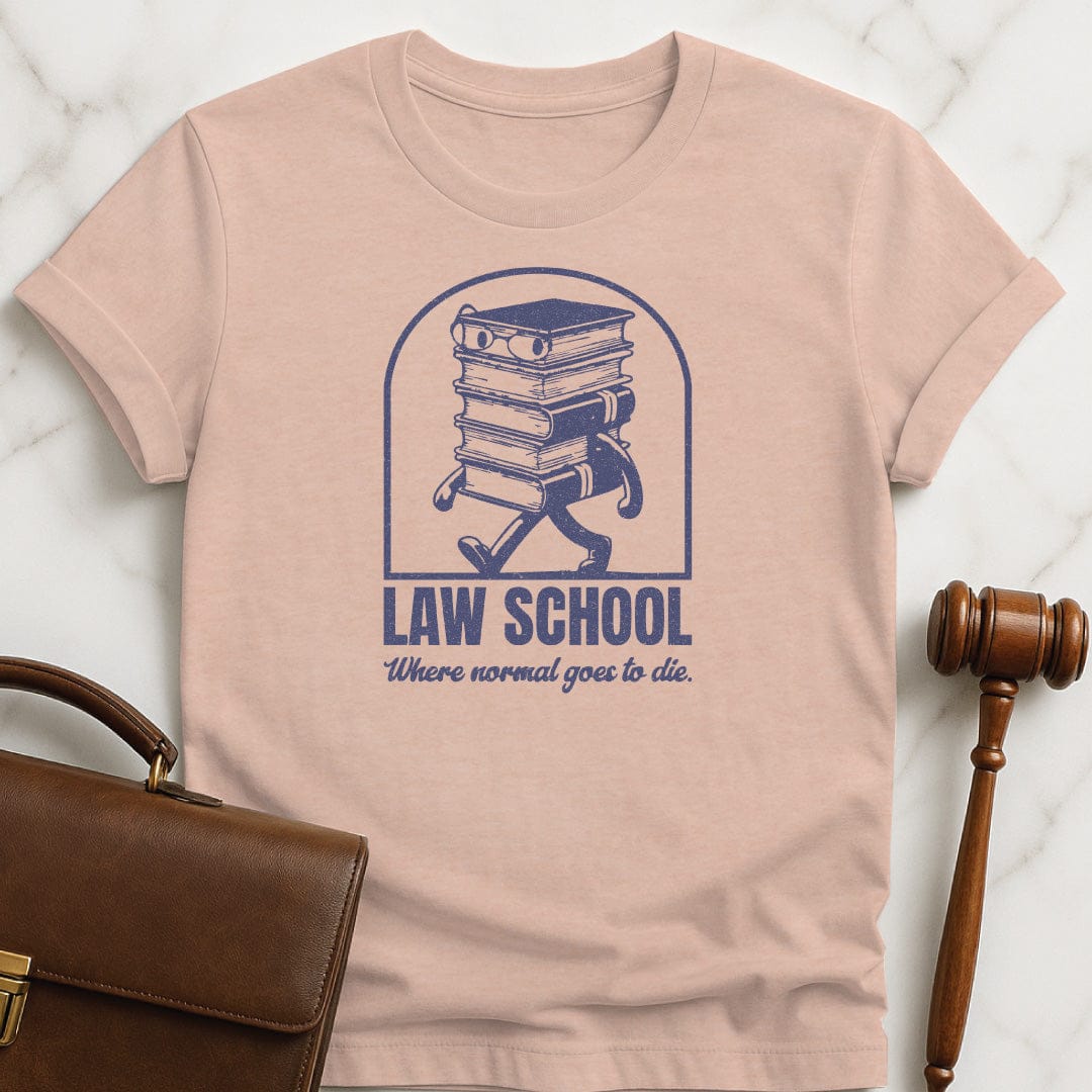 cool new lawyer tee that says Law School Where Normal Goes to Die featuring pile of books with a face in heather peach