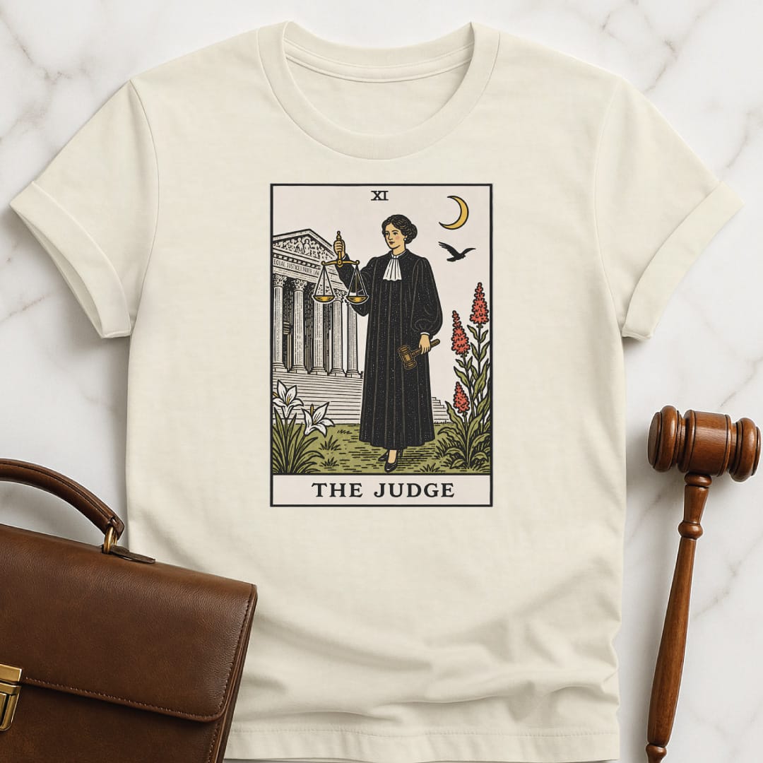cool law school t-shirt that says The Judge featuring tarot card style of a woman judge holding a scales of justice and gavel in front of courthouse in cream