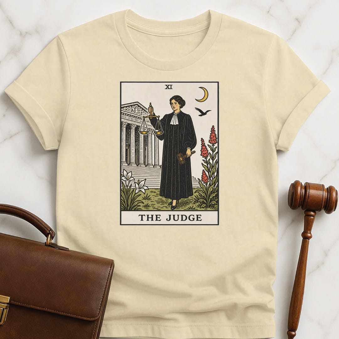 trendy law student t shirt that says The Judge featuring tarot card style of a woman judge holding a scales of justice and gavel in front of courthouse in cream
