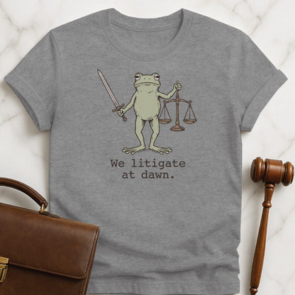 cool new lawyer graphic tshirt that says We litigate at dawn featuring frog with a sword and scales of justice in grey
