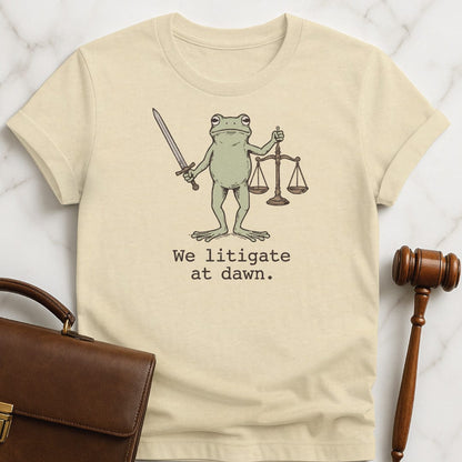 cool law school tshirt that says We litigate at dawn featuring frog with a sword and scales of justice in cream