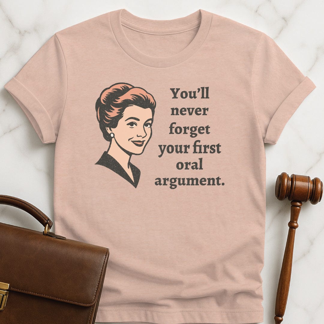 funny new attorney graphic t-shirt that says You Never Forget Your First Oral Argument featuring A retro woman in heather peach